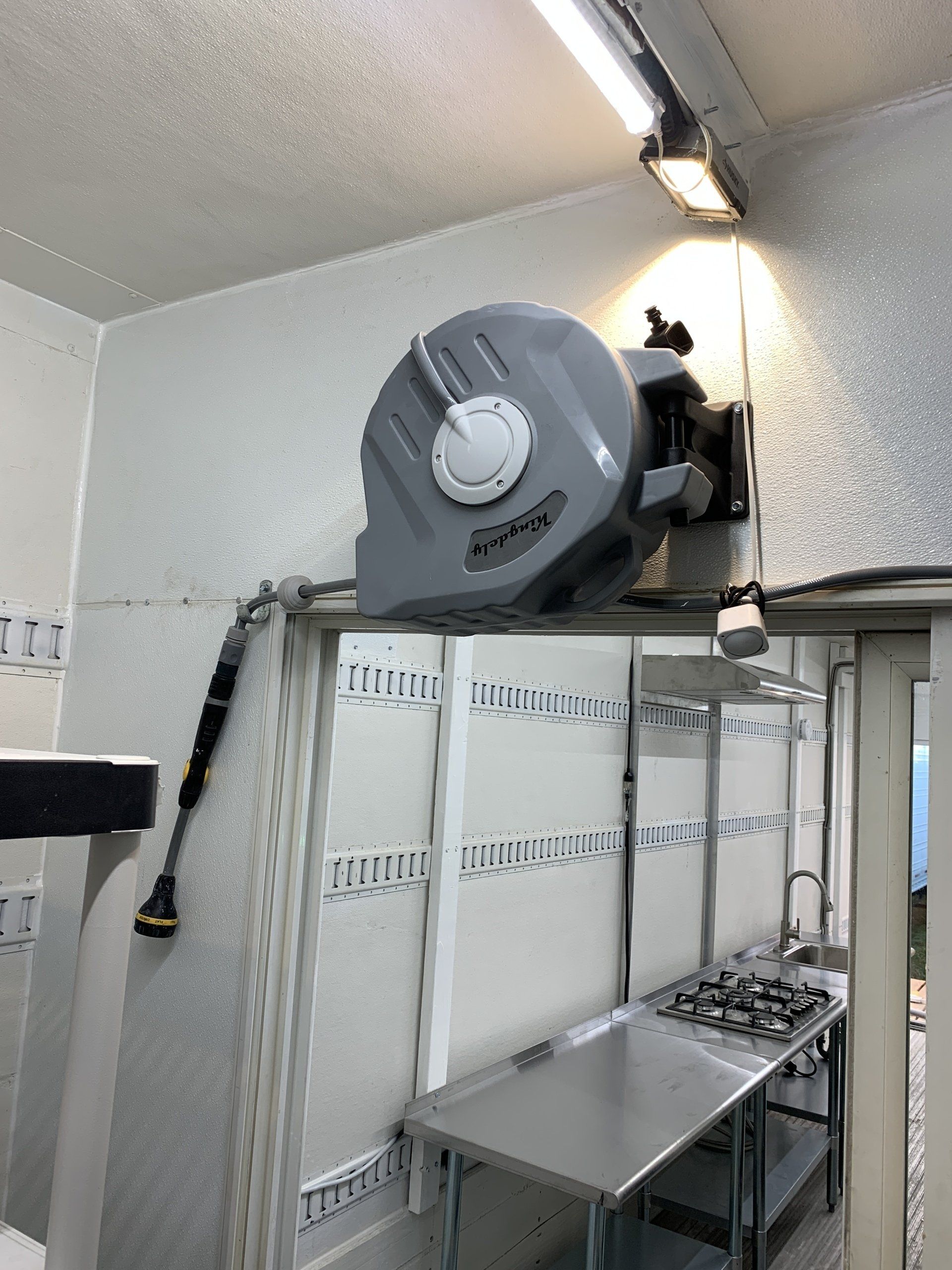 Industrial room with a large gray wall fan above stacked panels and a metal workbench under bright lights