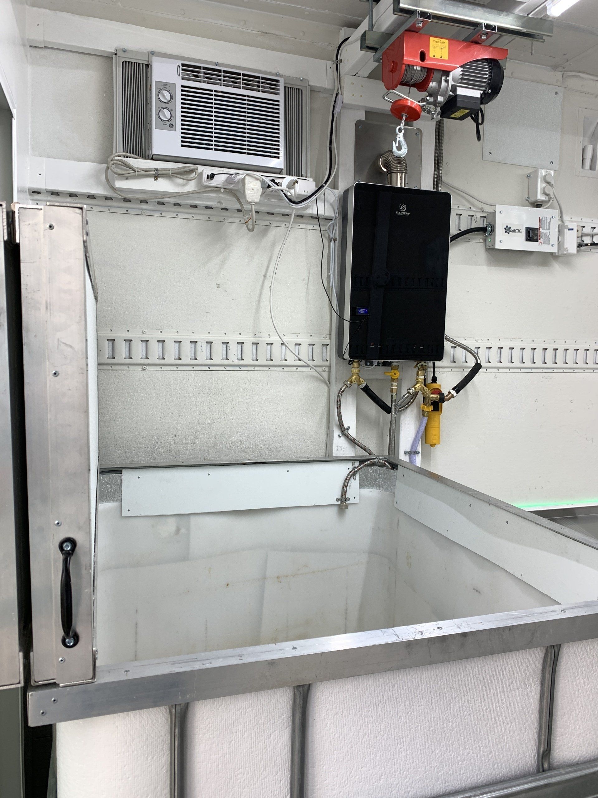 Industrial sink with wall-mounted vent, black control box, and pipes in a utility room