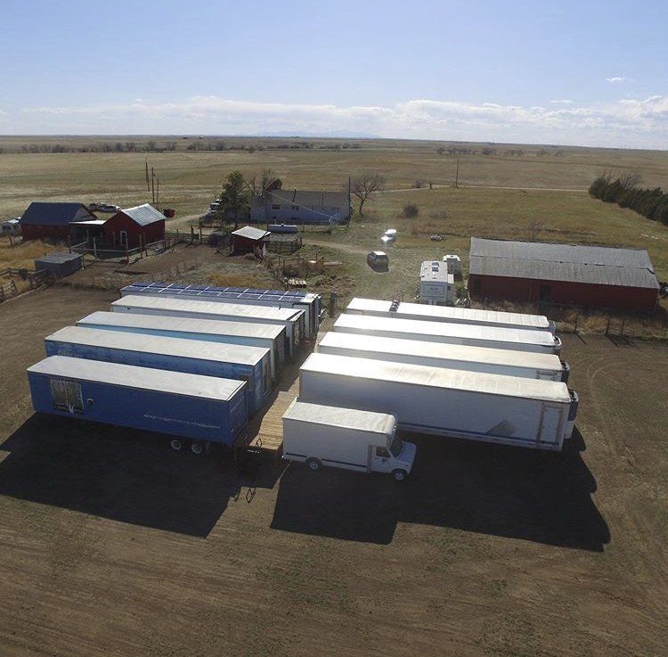 Rural farmyard with several white and blue trailers and red barns under a wide open sky