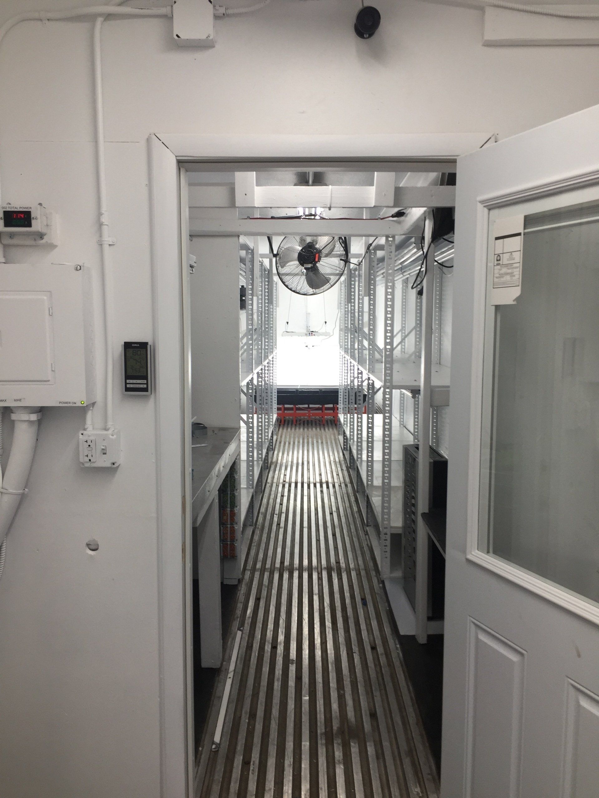 Narrow metal walkway in an industrial interior with white walls and open doors on both sides.