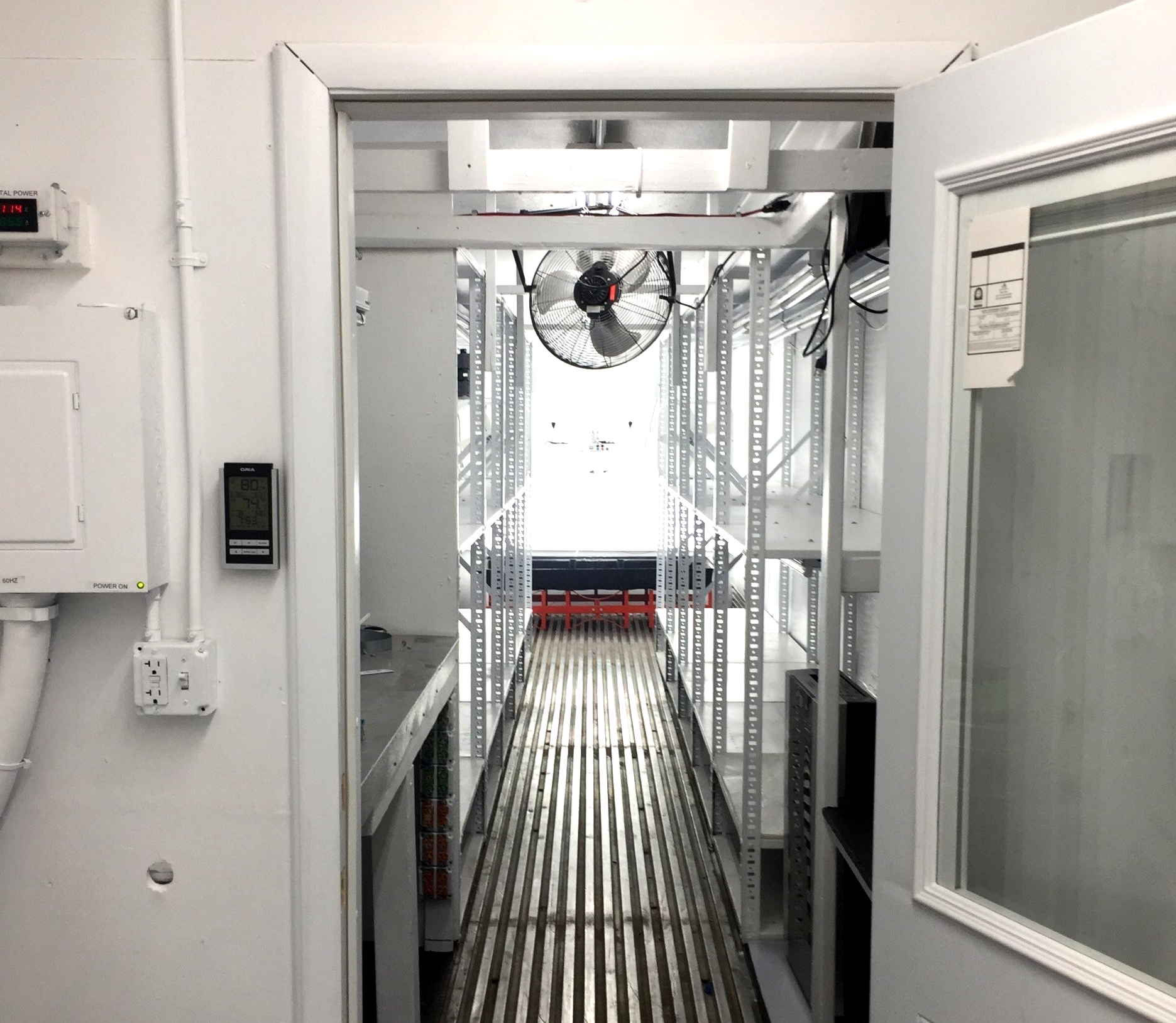 Narrow white corridor with metal shelving and a fan at the far end