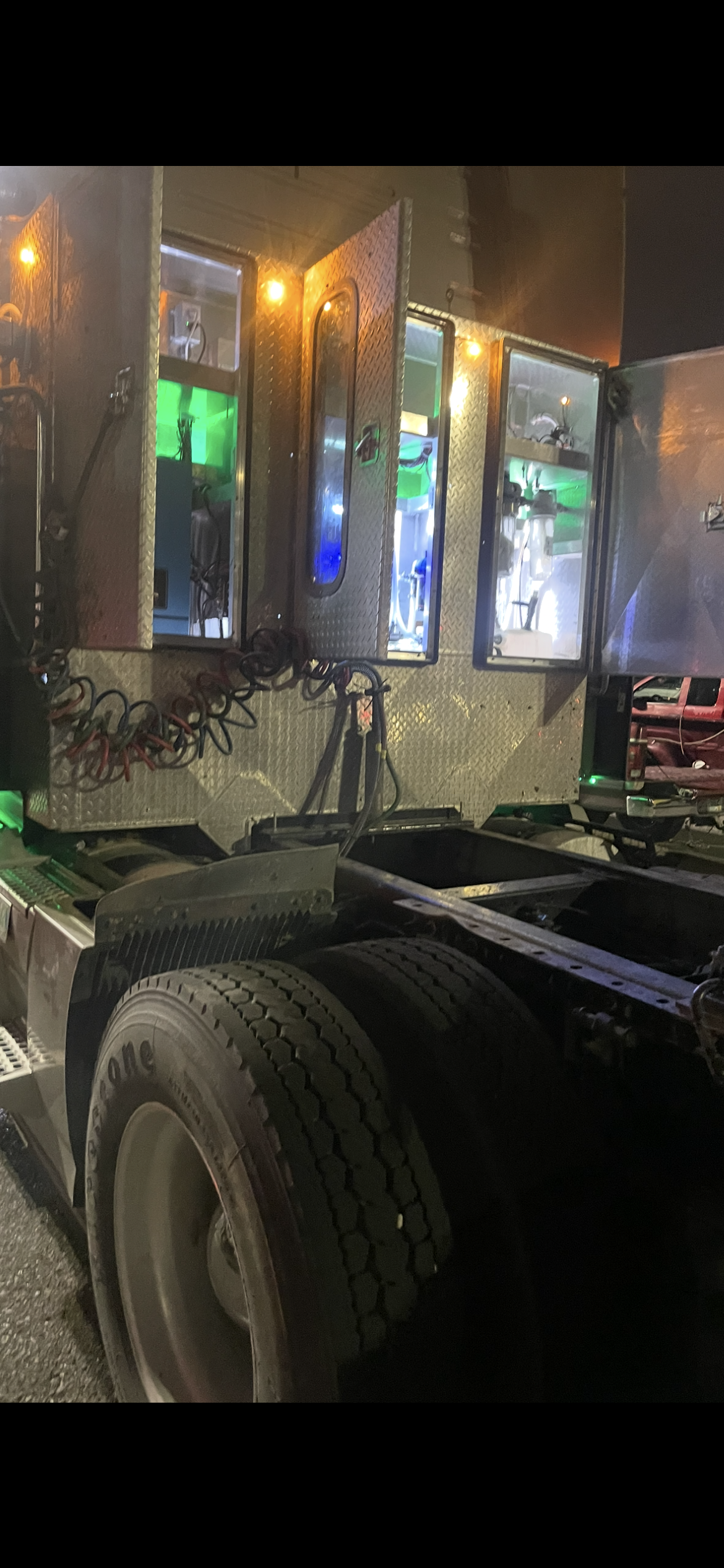 Semi-truck at night with illuminated chrome side panels and large tires parked on a wet street