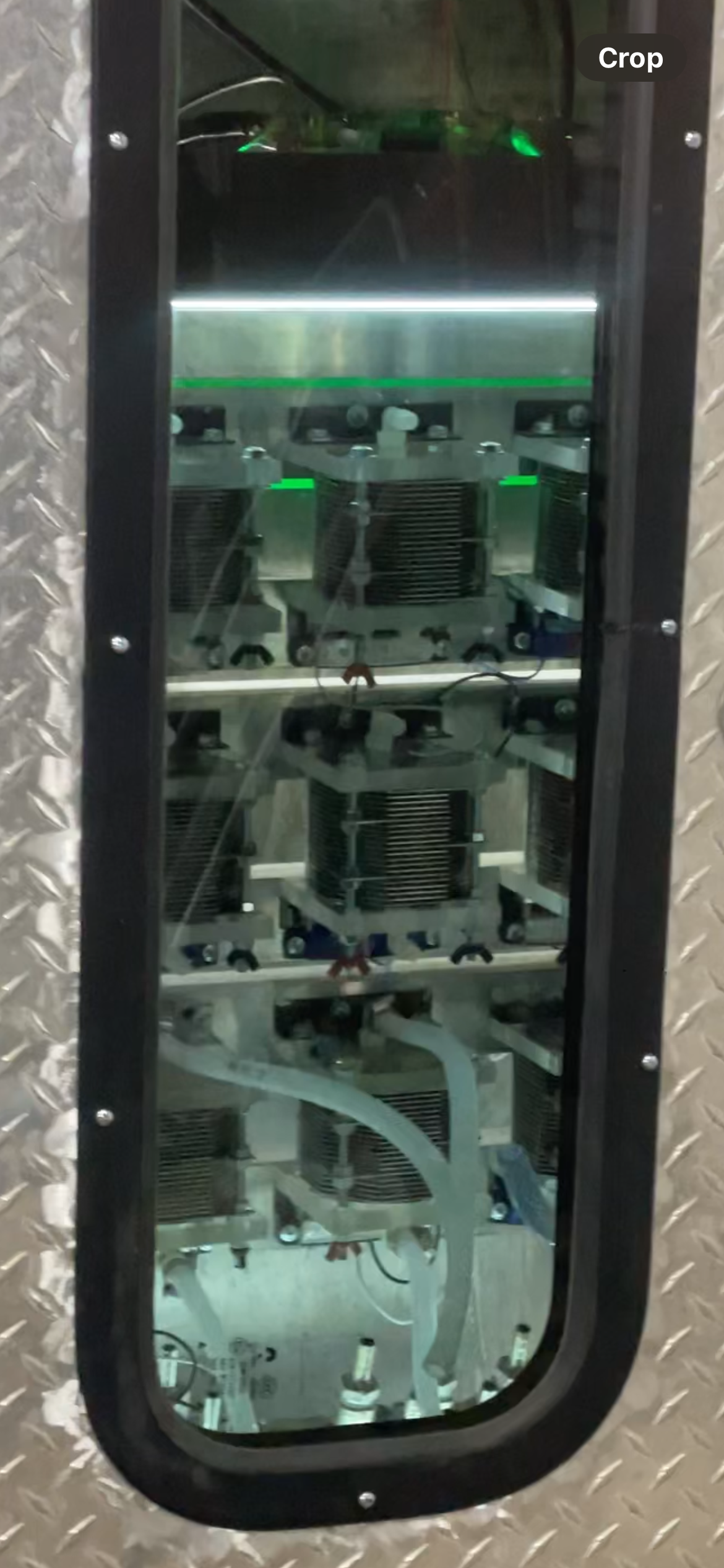View through a narrow window into a machine’s internal components with wires and metal parts lit green.
