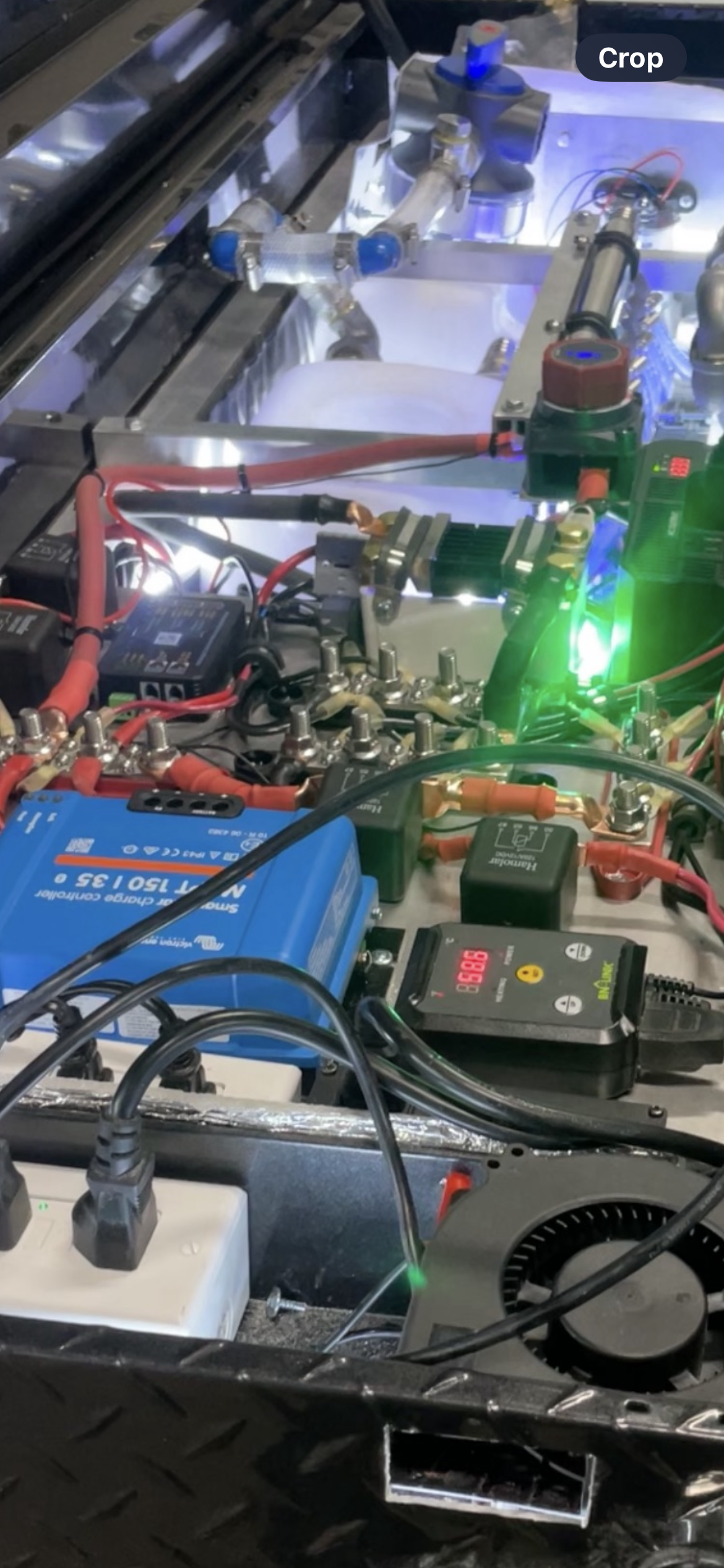 Close-up of a cluttered electronics workbench with wires, circuit boards, and a green status light.