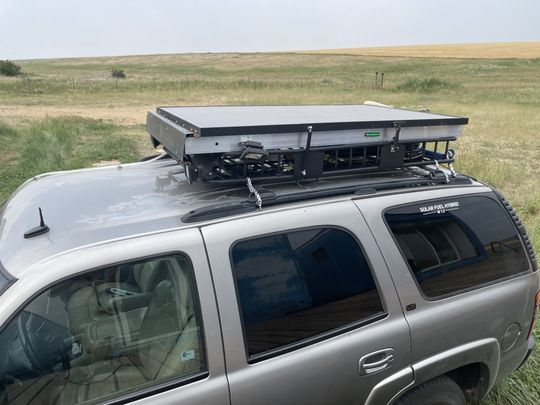 Silver SUV with rooftop cargo box parked on a grassy plain under a cloudy sky