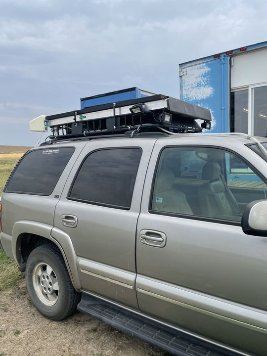 Silver SUV with roof cargo rack parked beside a blue trailer in an open field