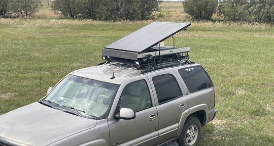 Gray SUV with an open rooftop cargo box parked on grass near trees
