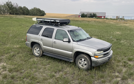 Silver SUV parked on grassy field with a roof cargo box in the background.