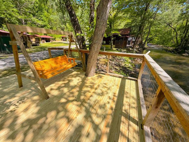 Wooden bridge over a creek, with a swing in the middle, surrounded by trees and greenery.