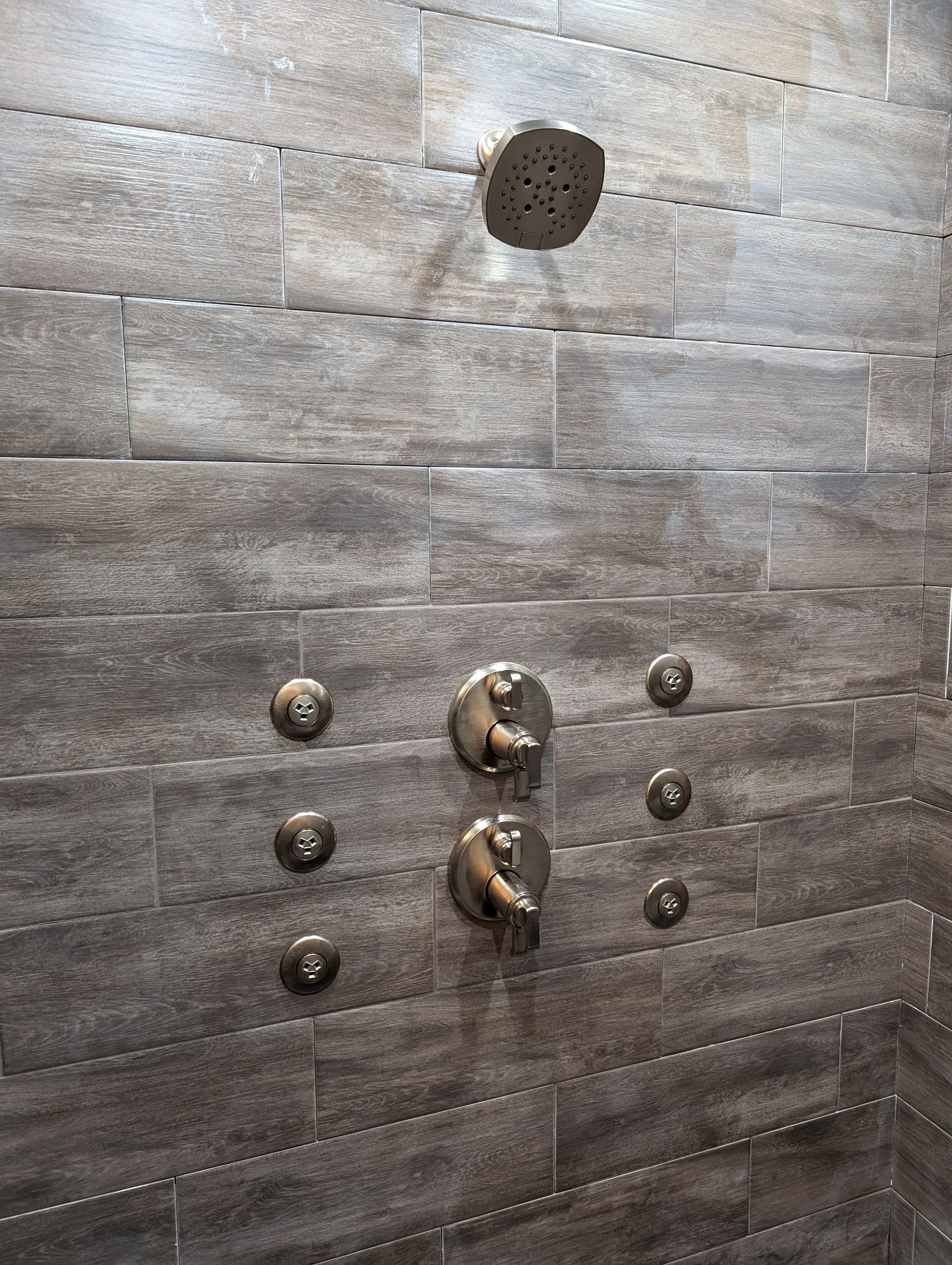 Dark tiled shower wall with metal knobs and a circular showerhead opening