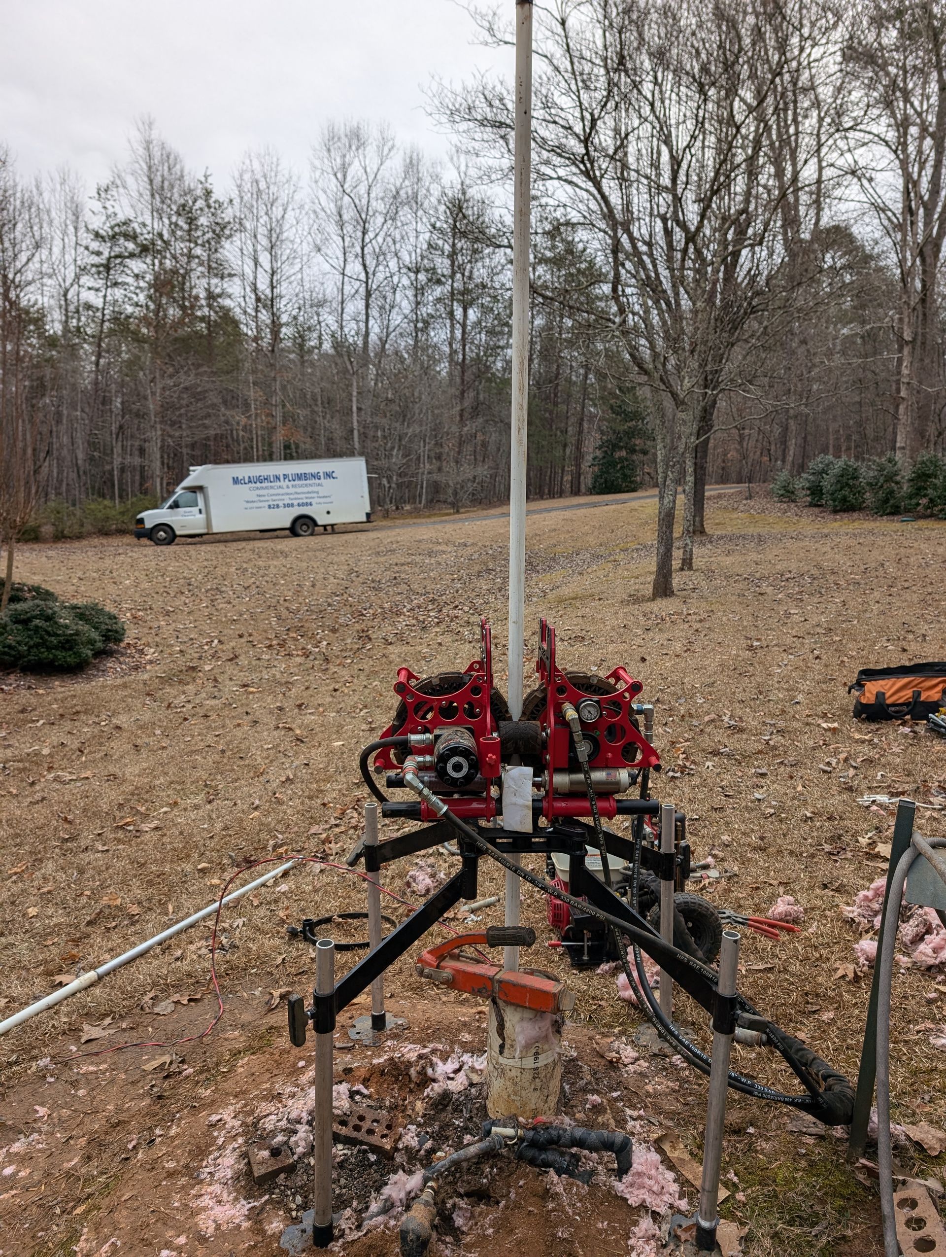 Red farm machine in a leaf-covered yard with a white truck and bare trees in the background