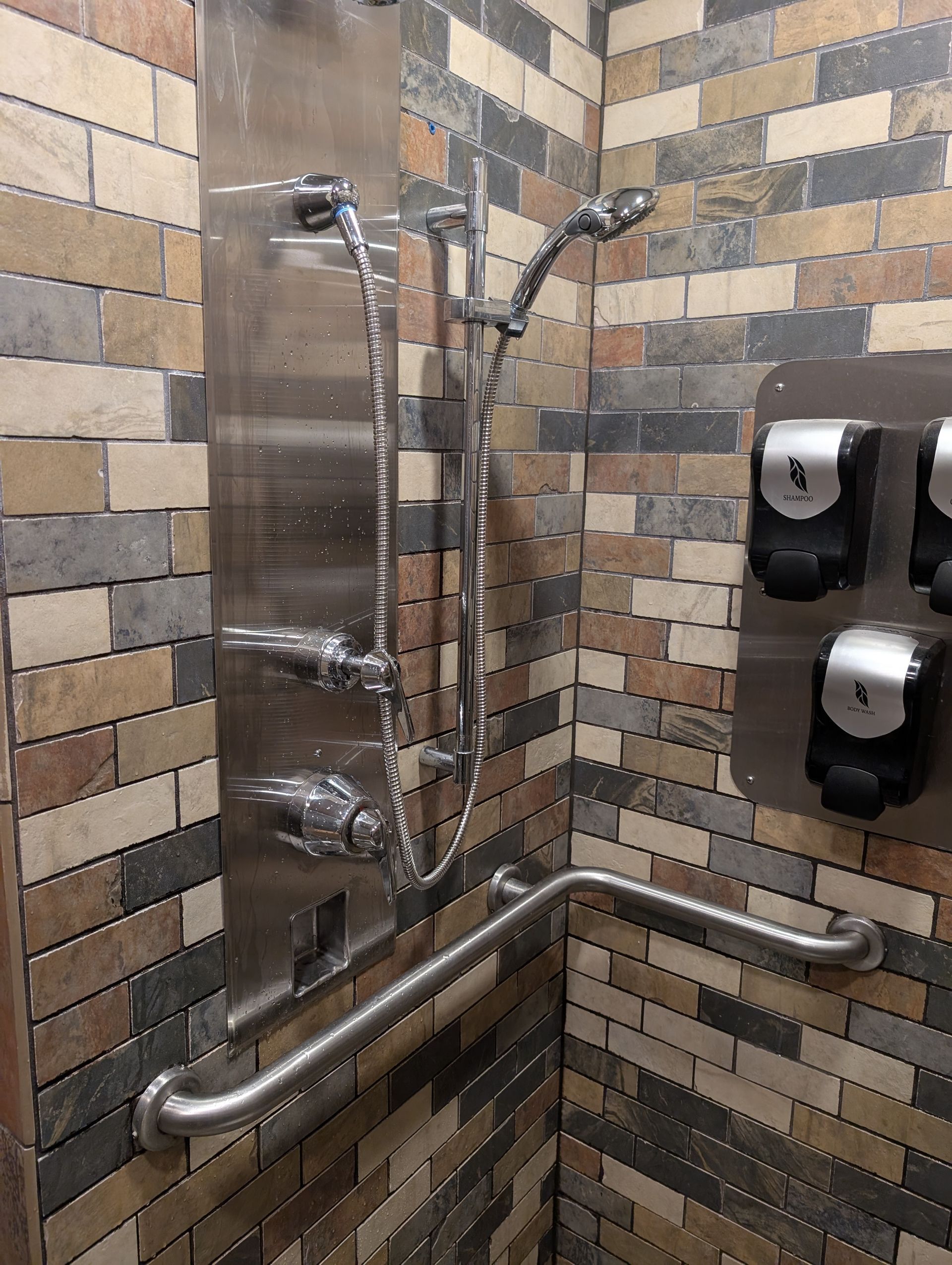 Accessible shower stall with grab bars, handheld showerheads, and wall-mounted dispensers on tiled walls