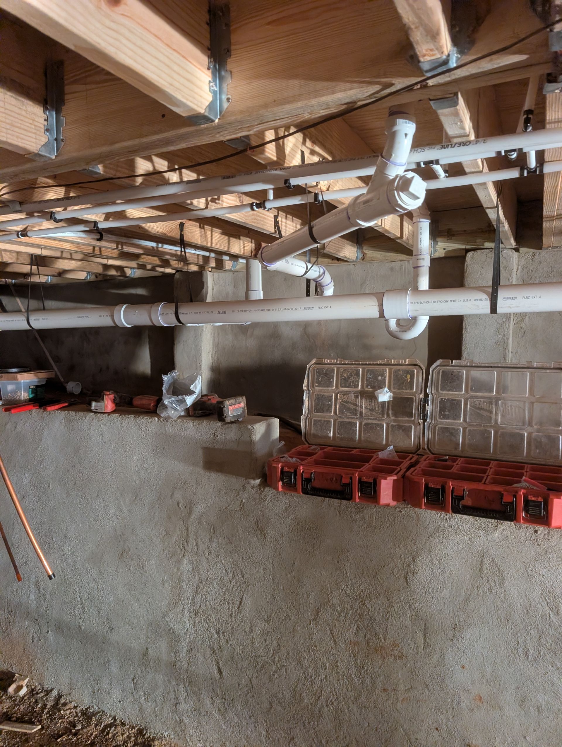 Basement ceiling with exposed wooden beams, pipes, and a concrete wall with stacked red crates.