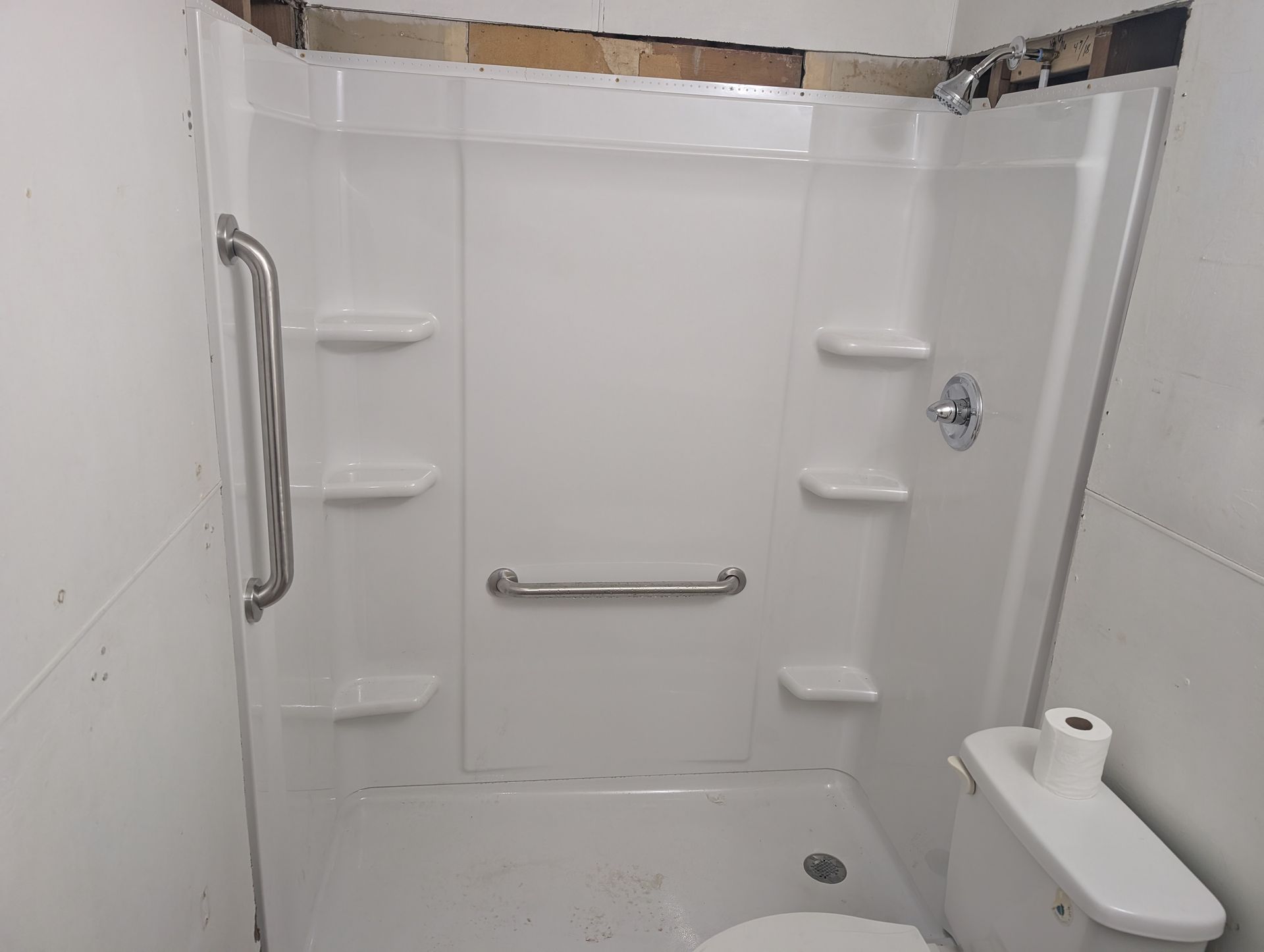 Accessible shower stall with grab bars, fold-down seat, and handheld showerhead