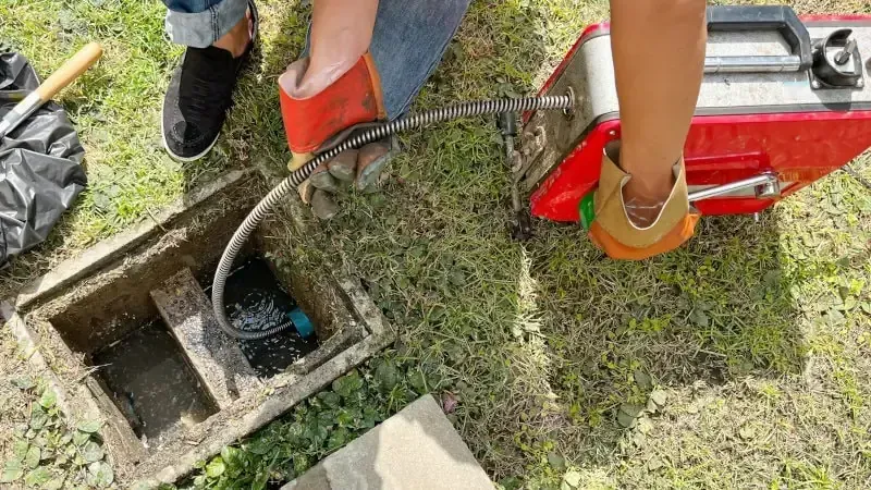 Workers using a red hose and tools to inspect a concrete utility pit in grassy ground Workers using a red hose and tools to inspect a concrete utility pit in grassy ground