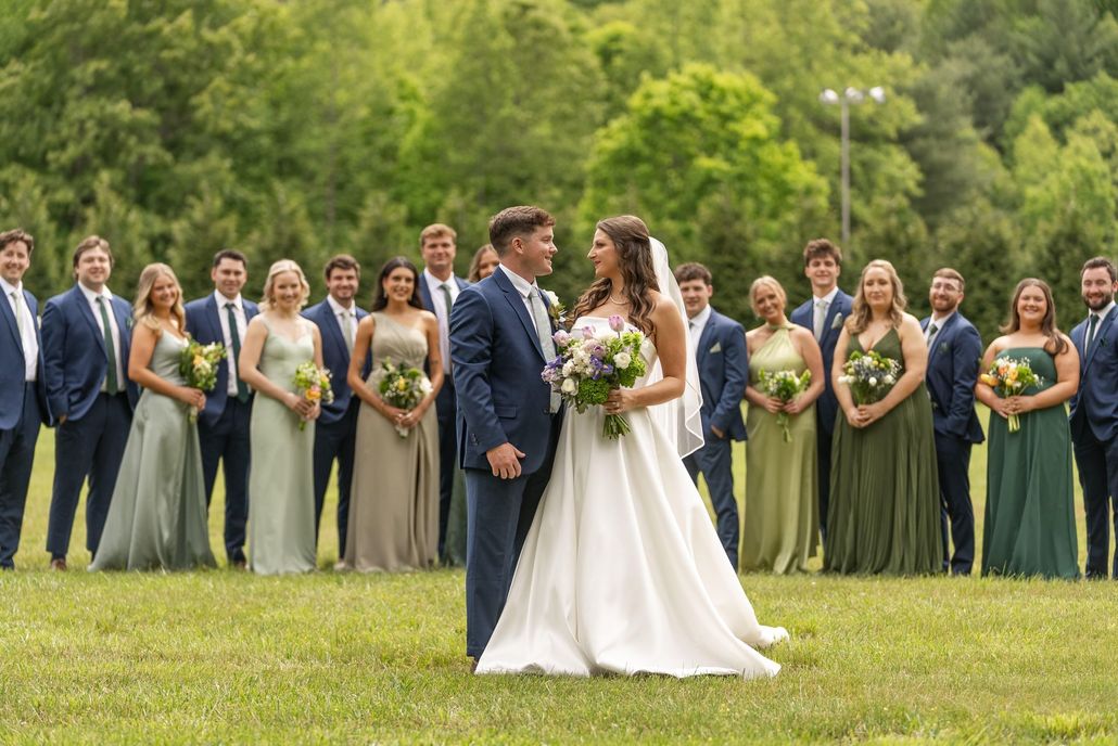 Bride and groom with wedding party; green field setting.