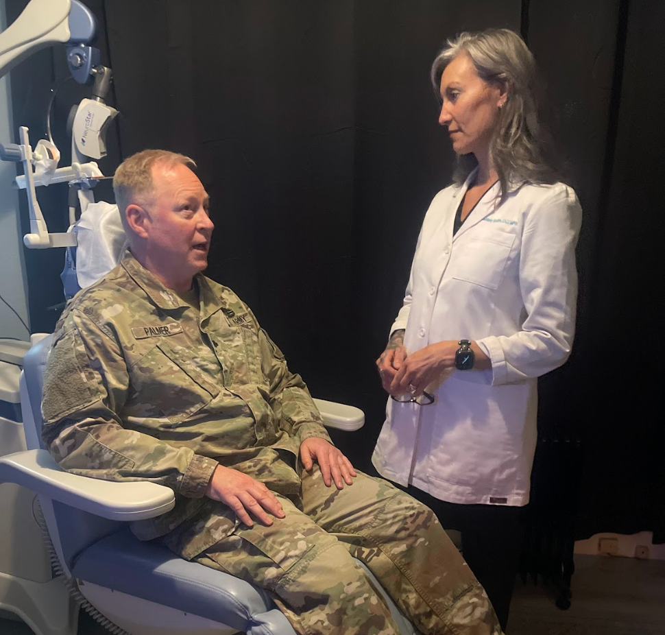 Military man seated in a dental chair talks with a clinician in a white coat.