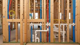 Framed house wall with exposed plumbing, pipes, and colorful electrical wiring under construction