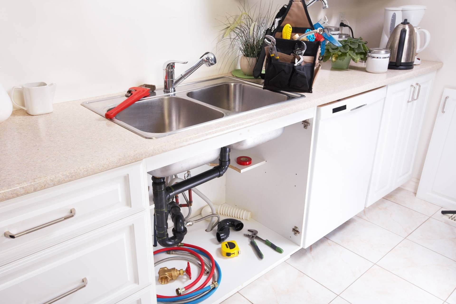 Bright kitchen sink area with tools and exposed plumbing under the counter