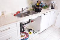 Bright kitchen sink area with tools and exposed plumbing under the counter