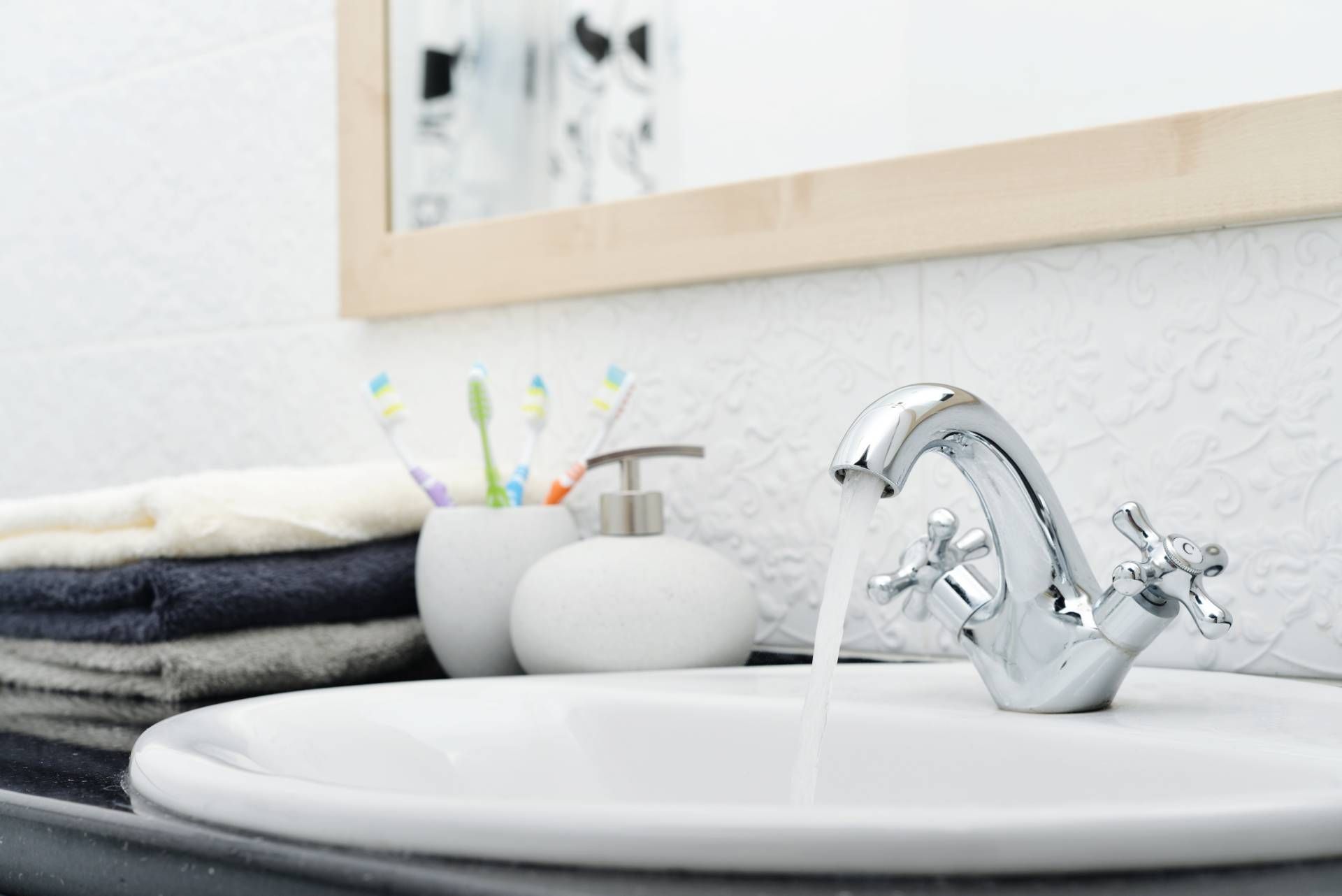 Chrome bathroom faucet and white sink with folded towels and toiletries nearby