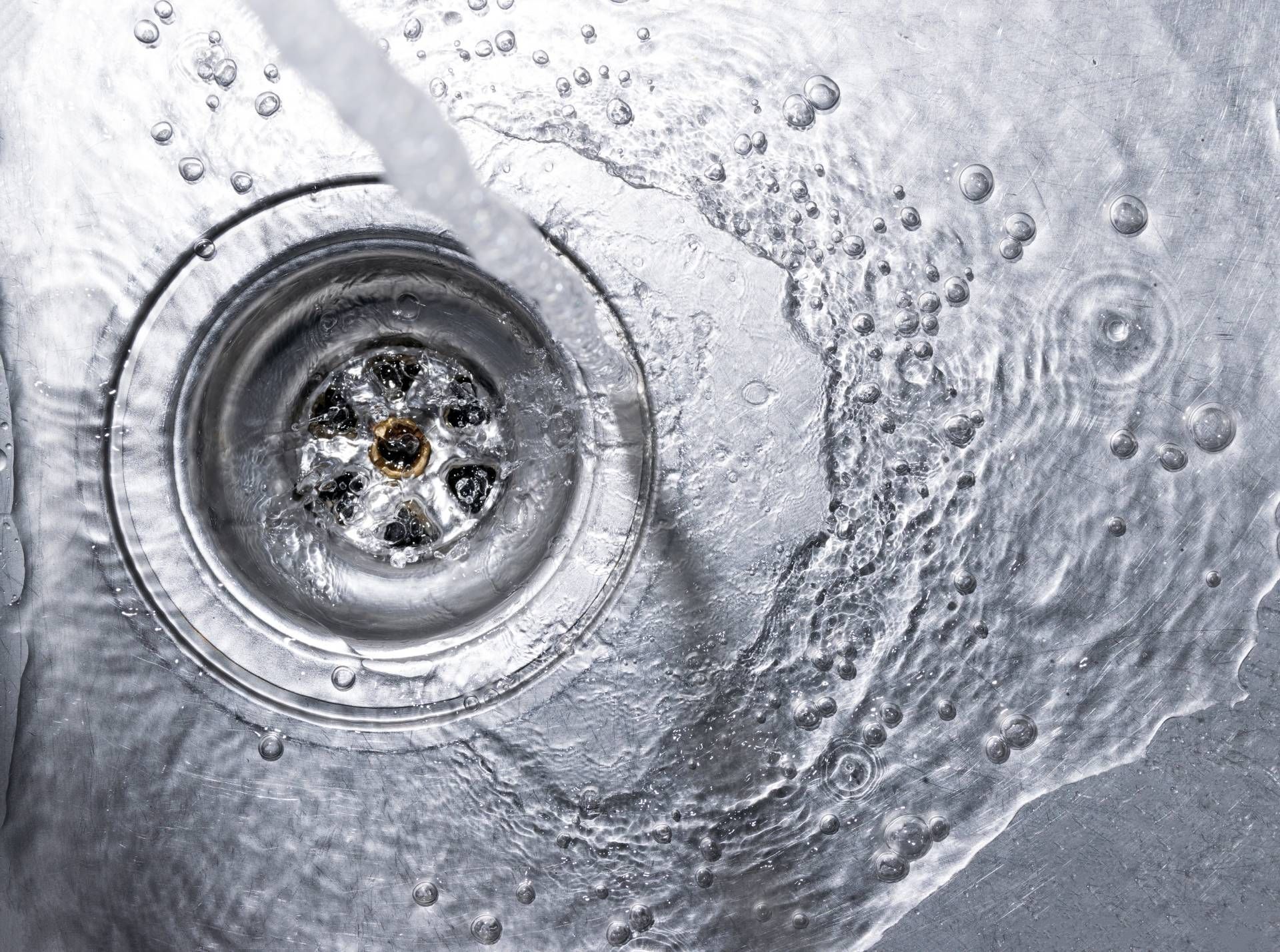 Close-up of a stainless steel sink drain with water swirling around it