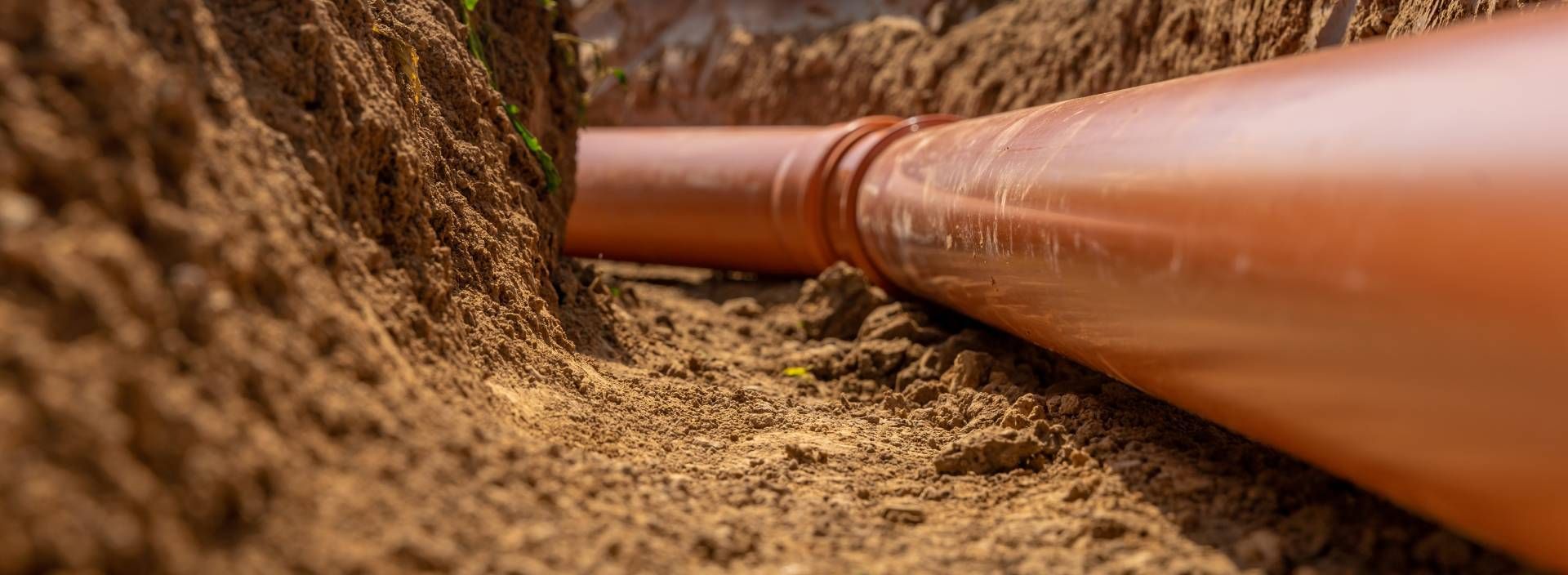 Orange pipeline running through a dirt trench in a construction site