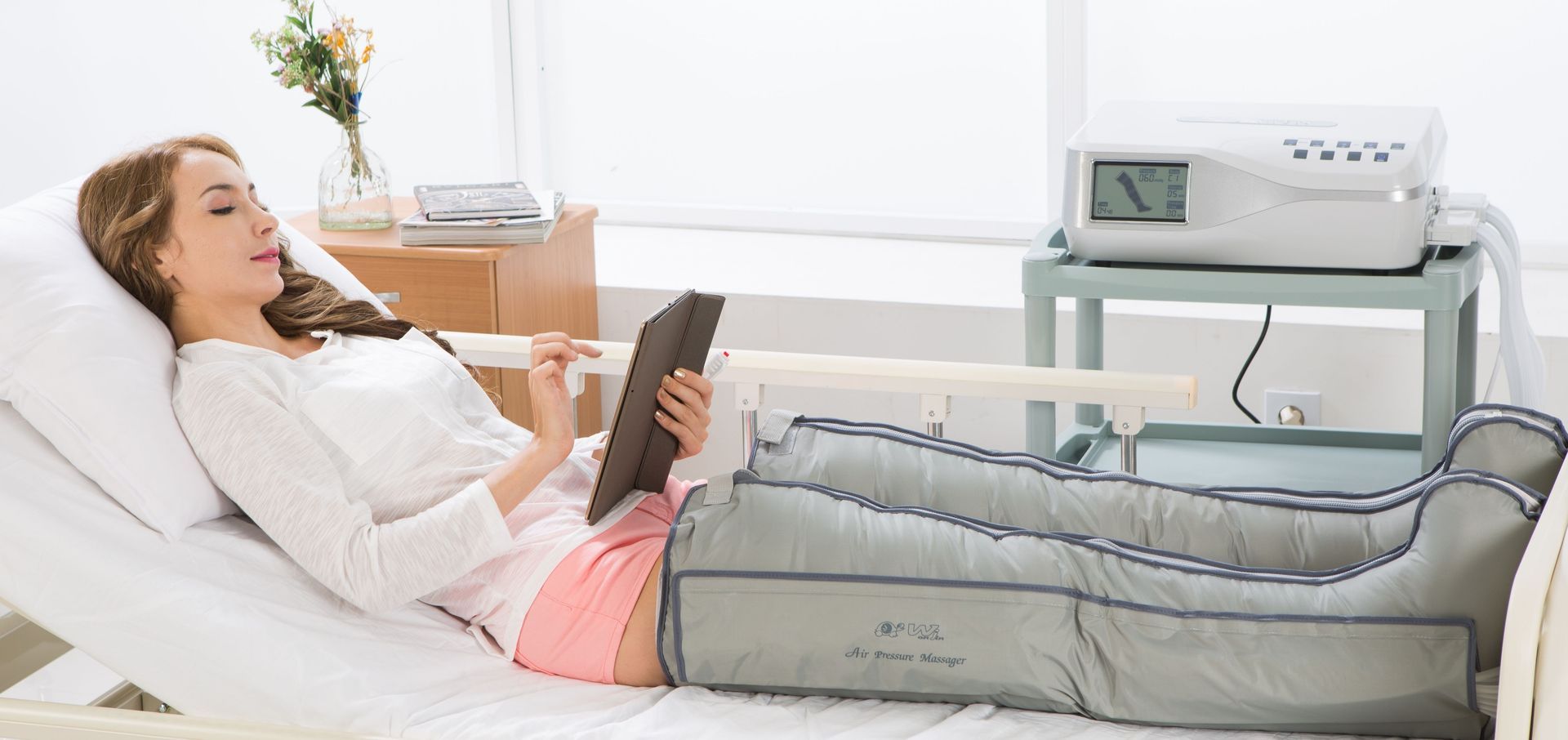 Eine Frau liegt in einem Krankenhausbett und nutzt ein Tablet.