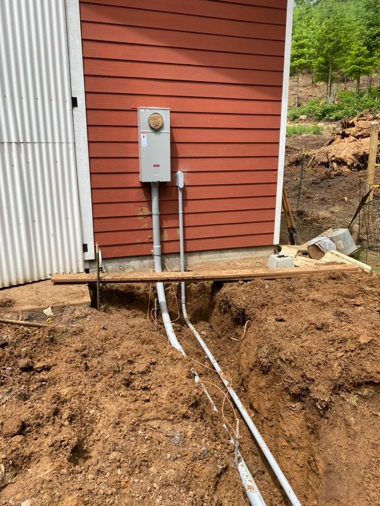 Electrical conduit buried in trench, near an electrical meter box on a red building.