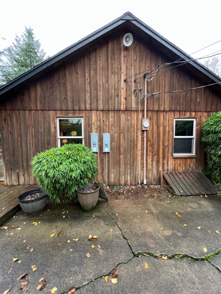Wooden building exterior with windows, electrical boxes, and a concrete patio.
