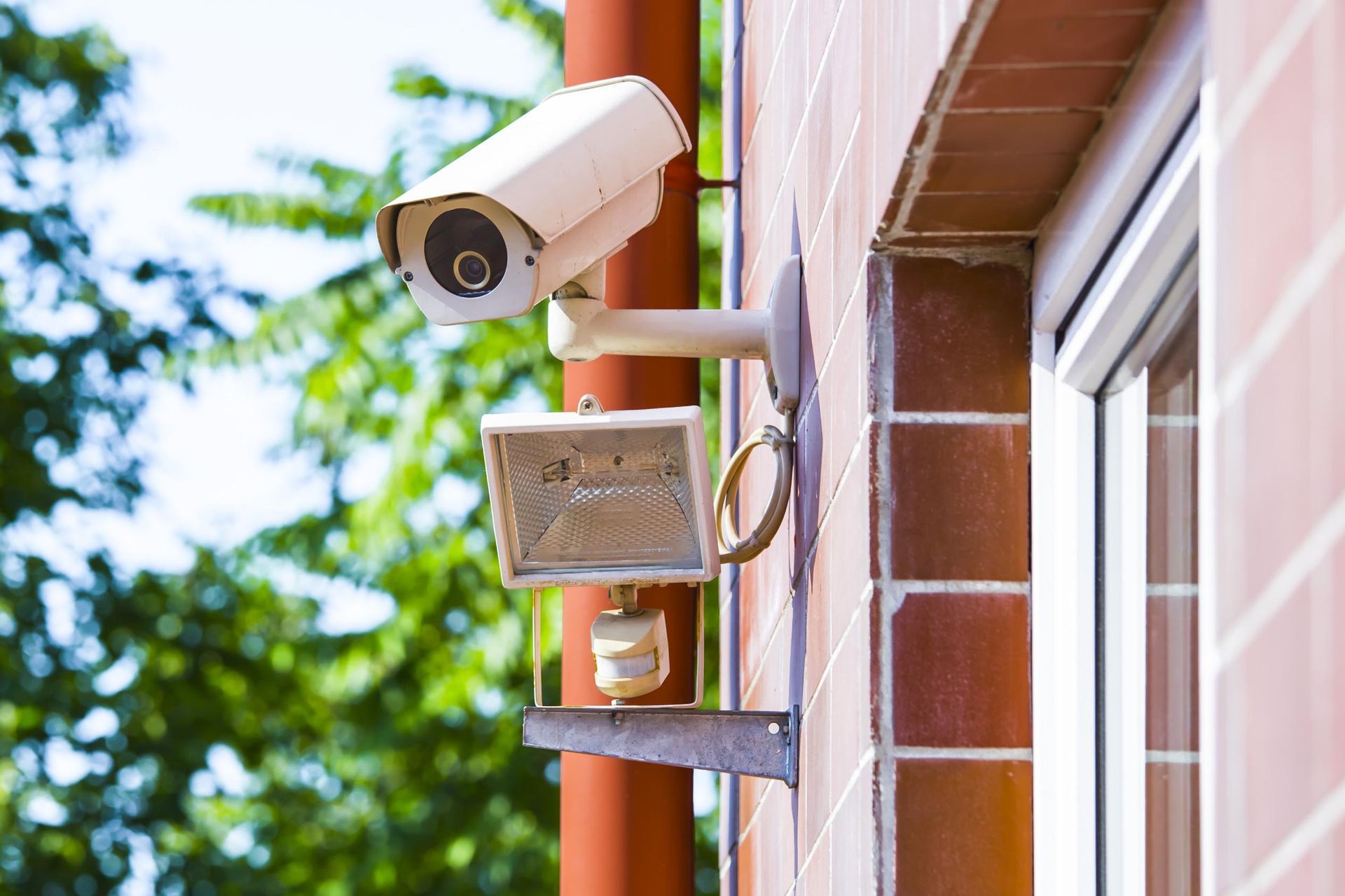 Security camera and floodlight mounted on a brick wall.