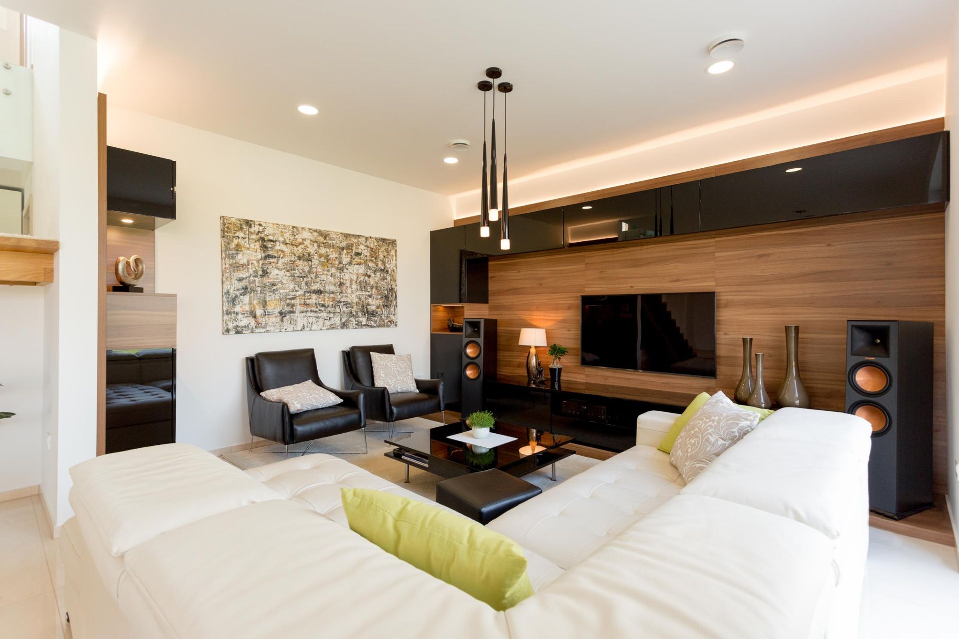 Modern living room with white sectional sofa, wood paneling, TV, and black leather chairs.