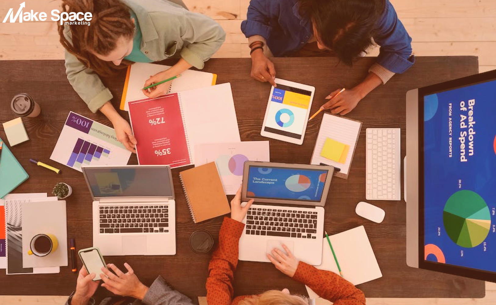 A group of people are sitting around a table with laptops and papers.