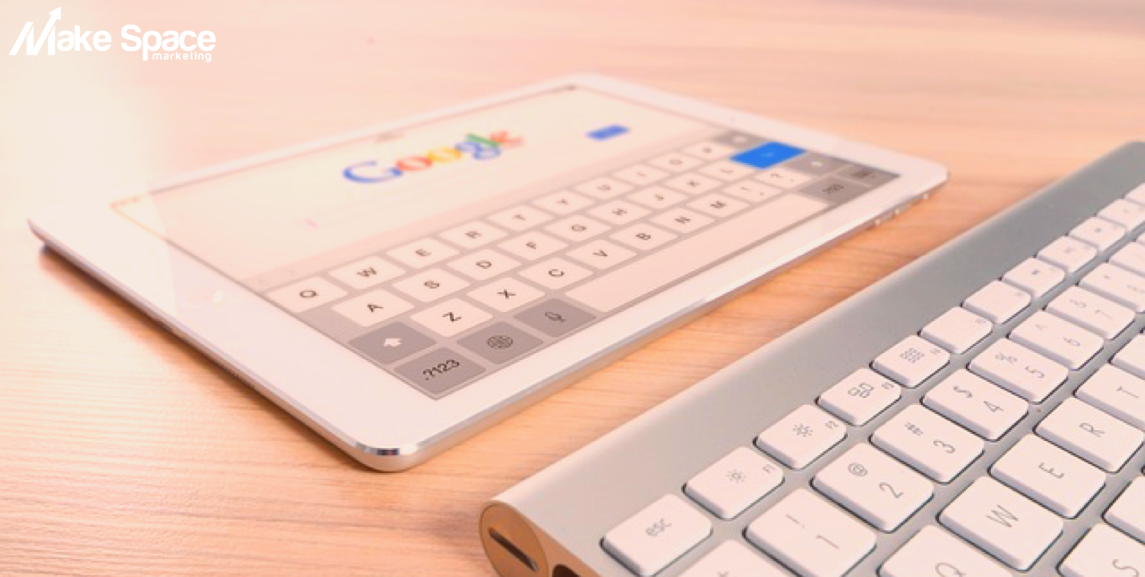 A tablet is sitting on a wooden table next to a keyboard.