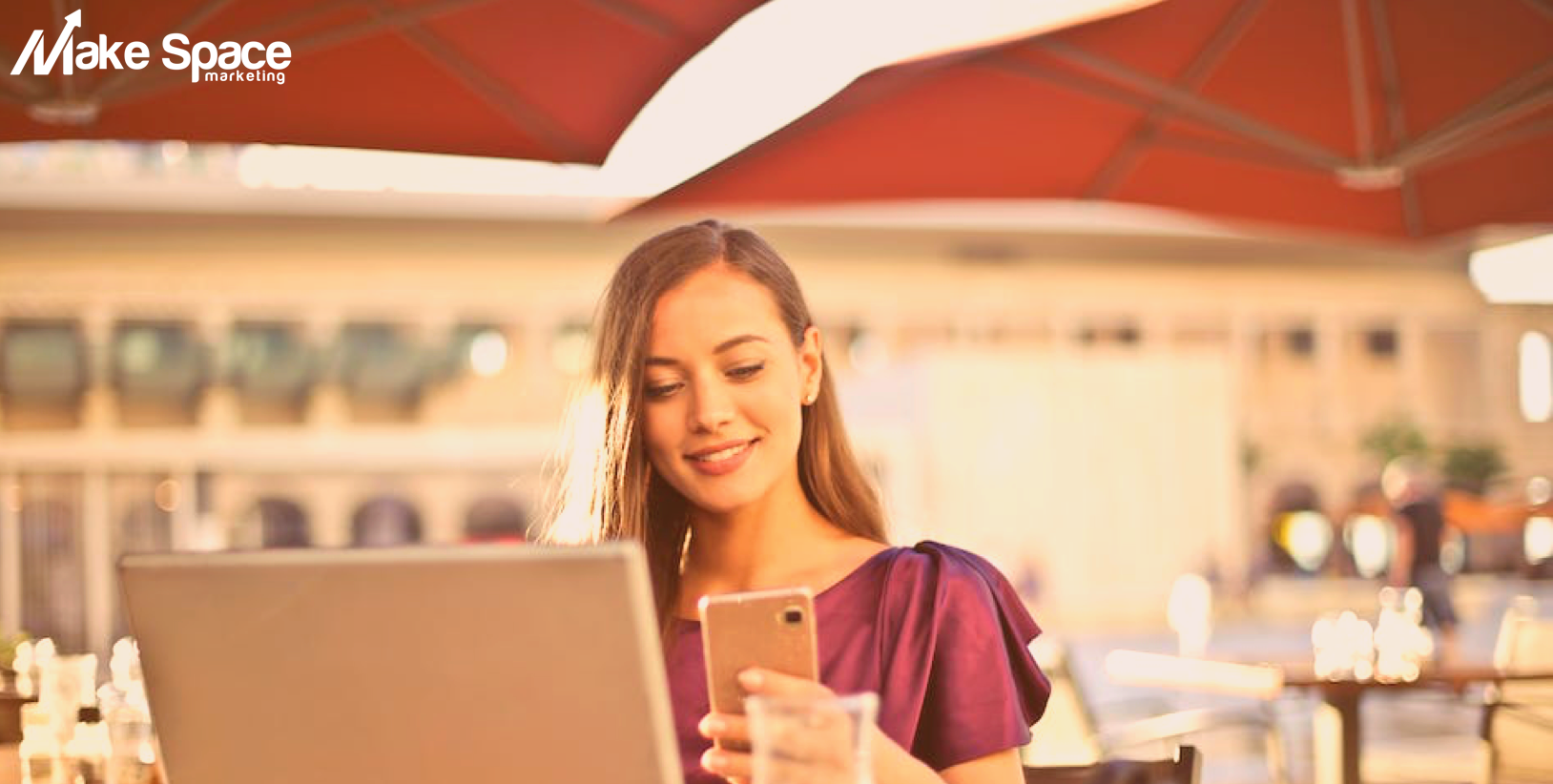 A woman is sitting at a table with a laptop and a cell phone.