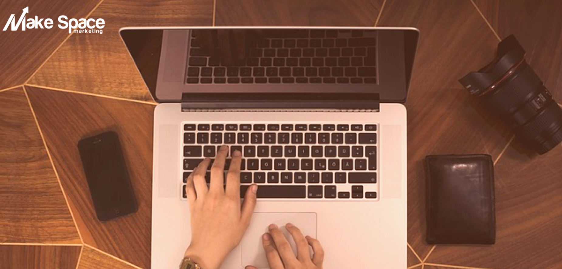 A person is typing on a laptop computer on a wooden table.