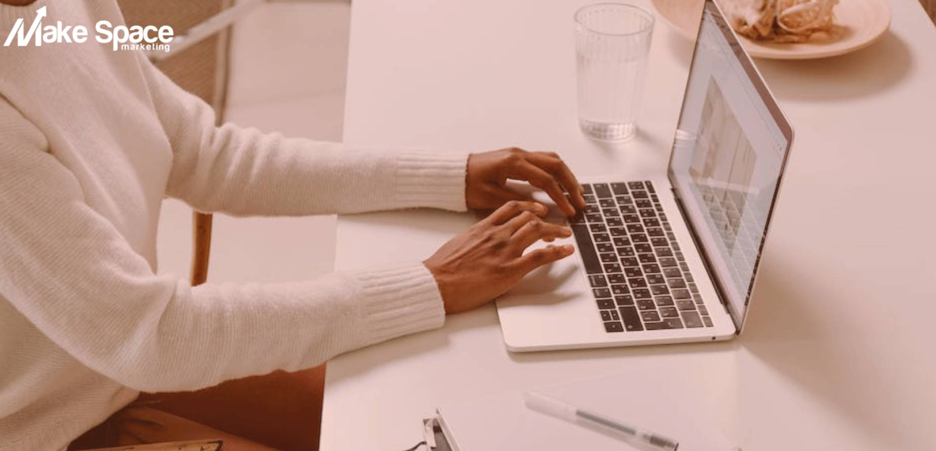 A woman is sitting at a table typing on a laptop computer.
