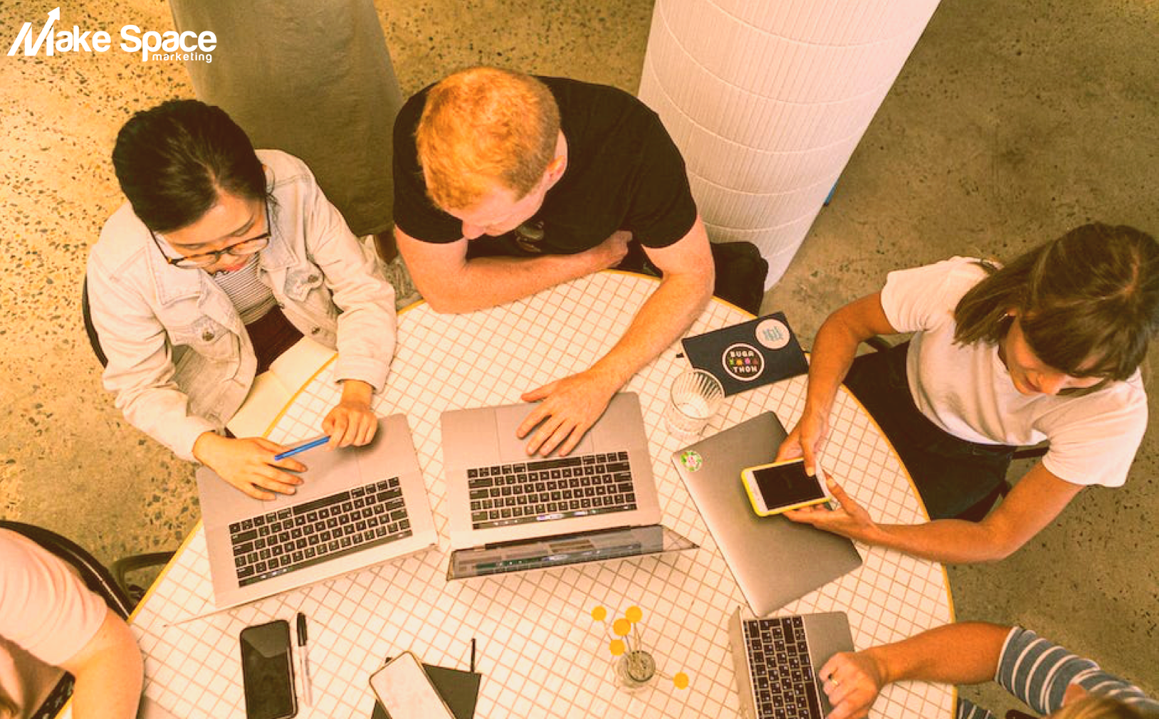 A group of people are sitting around a table with laptops.