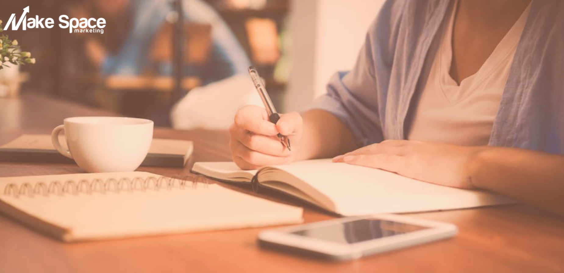 A woman is sitting at a table writing in a notebook.