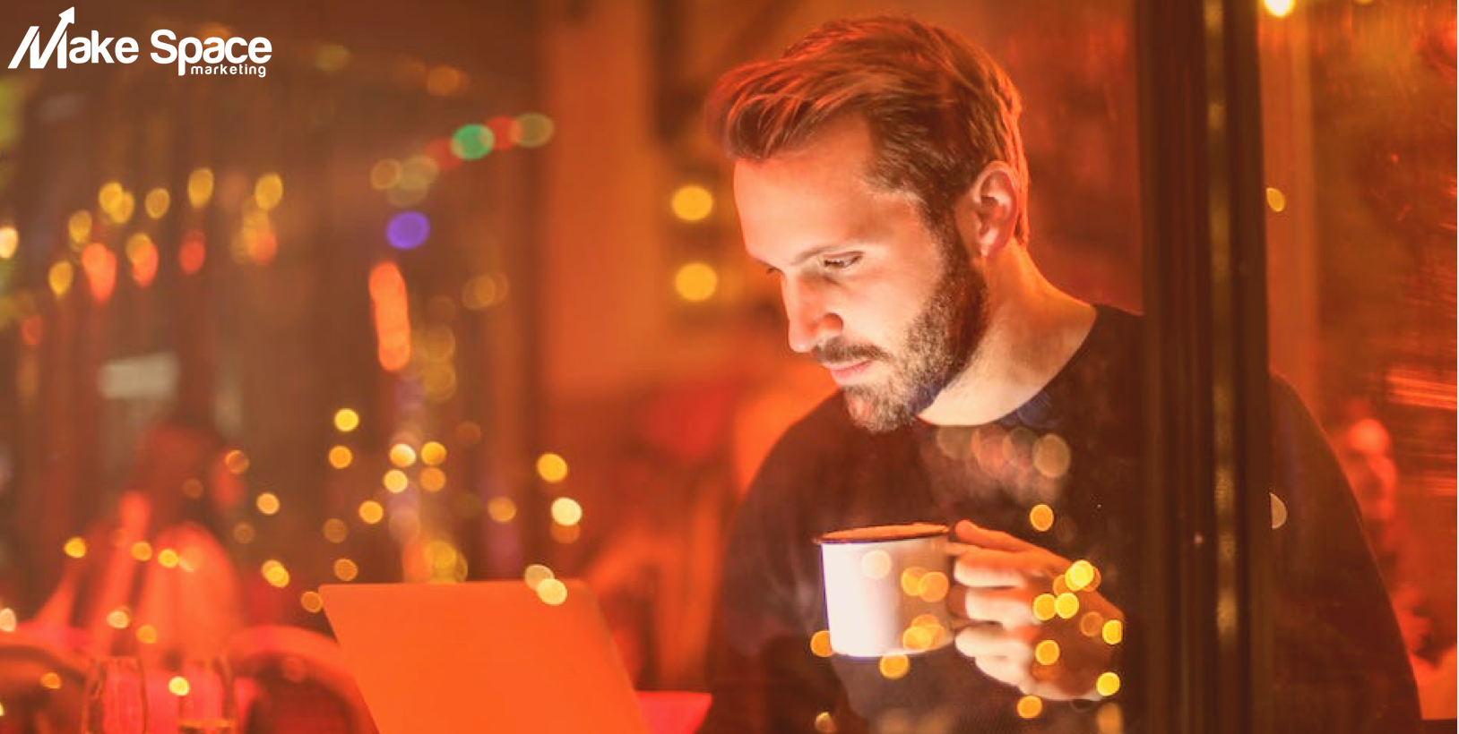 A man is drinking a cup of coffee while looking at a laptop.