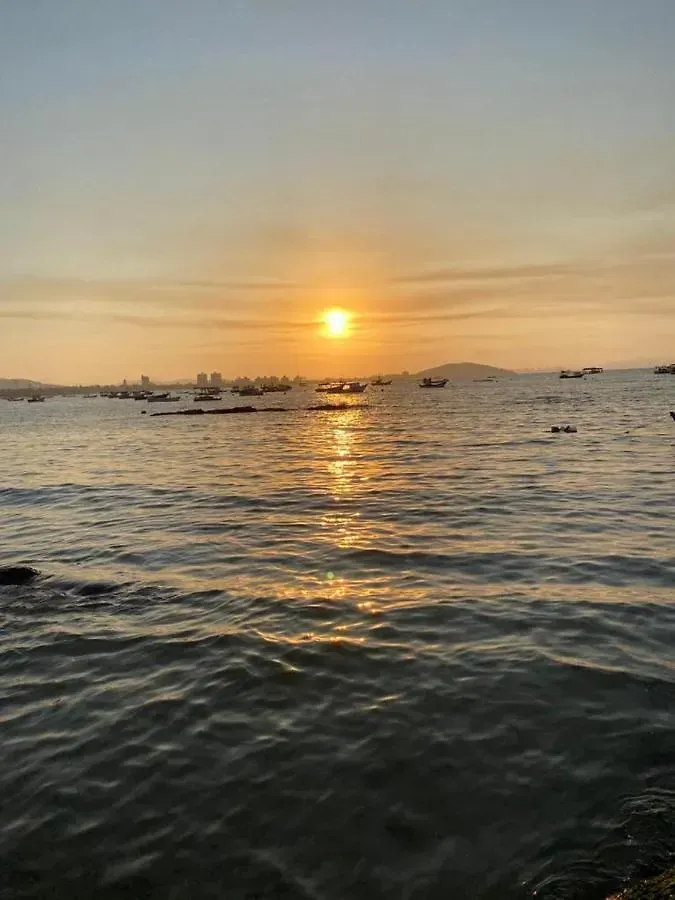 Pôr do sol sobre o oceano calmo, com pequenas embarcações silhuetadas no horizonte e reflexos dourados na água.