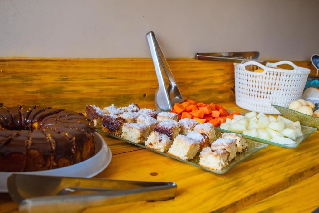 Buffet de sobremesas em mesa de madeira com fatias de bolo, doces com frutas e utensílios para servir.