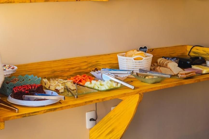 Mesa de buffet com frutas fatiadas, doces, pratos e utensílios sobre um balcão de madeira.