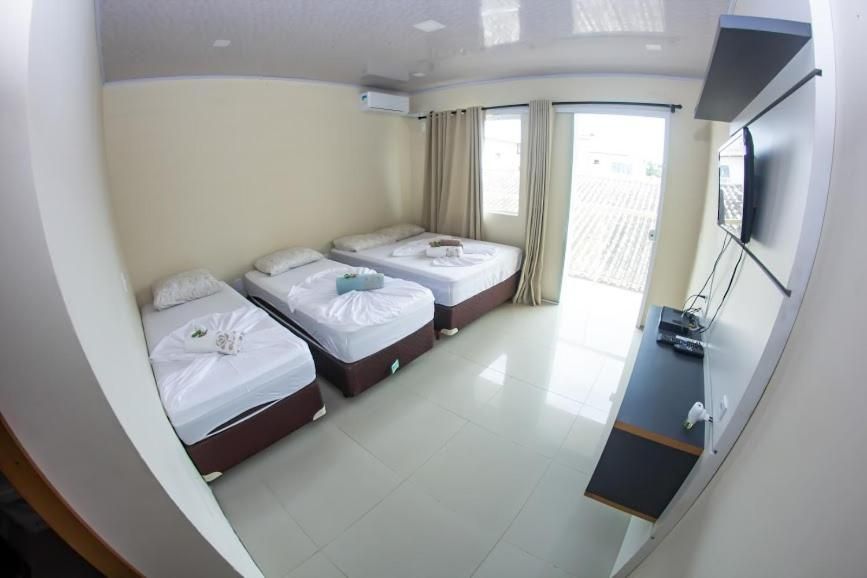 Quarto de hotel pequeno com três camas de solteiro, uma TV de parede e uma porta de varanda bem iluminada.