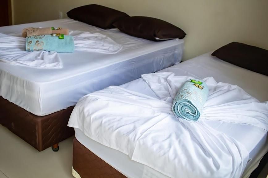 Duas camas arrumadas com lençóis brancos e toalhas enroladas em um quarto de hotel simples.