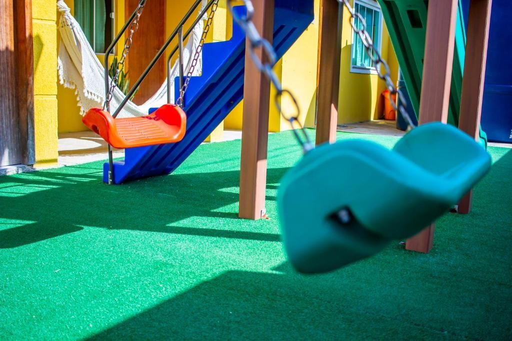 Parque infantil colorido com dois balanços em grama verde sob um sol radiante.