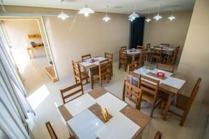 Pequena sala de jantar com várias mesas e cadeiras de madeira sob luminárias pendentes, vista de um canto.