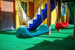 Parque infantil coberto e colorido, com balanços suspensos em grama verde e paredes em tons vibrantes de amarelo e azul.