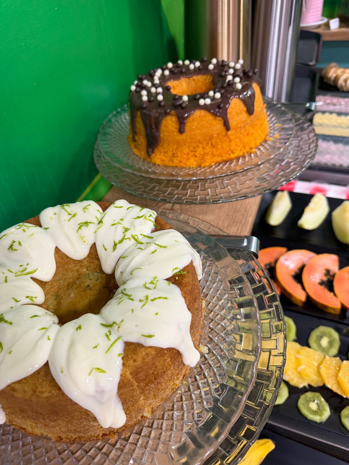 Dois bolos Bundt decorados em suportes de vidro, um com cobertura de chocolate e granulado, o outro com cobertura branca.