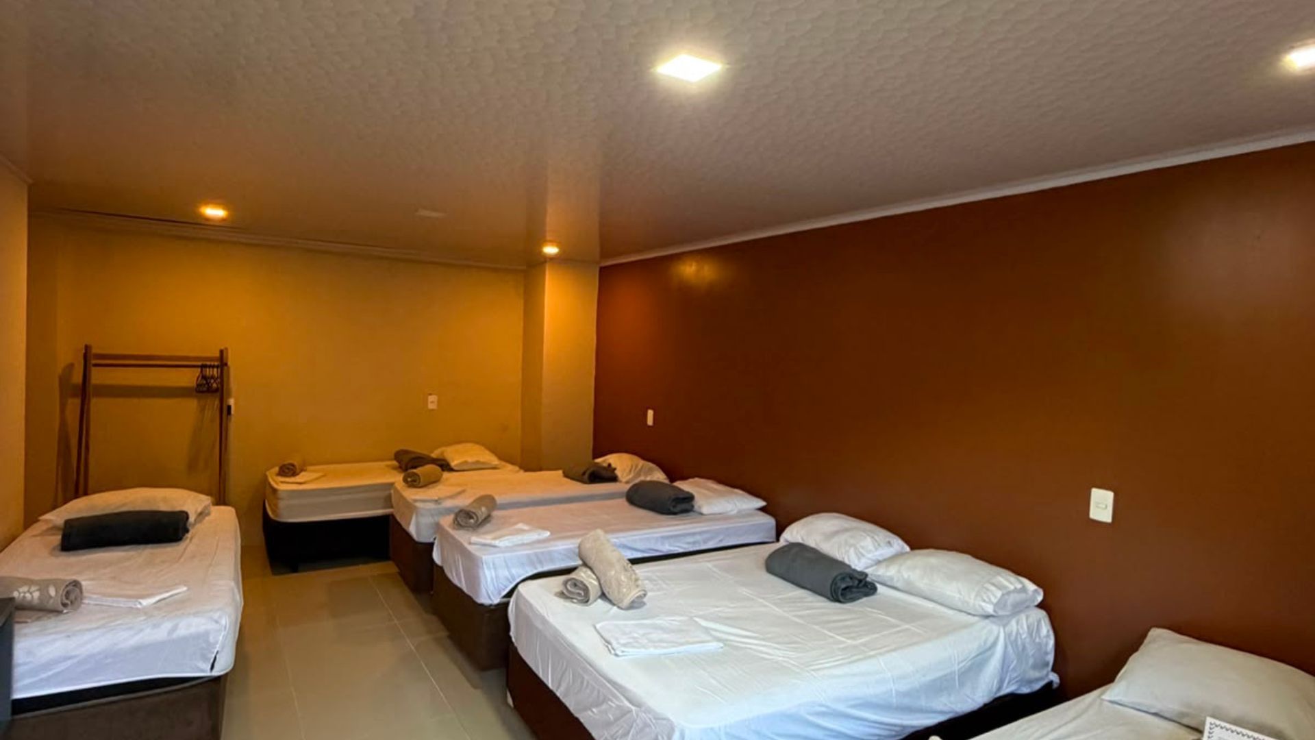 Quarto pequeno estilo dormitório com quatro camas de solteiro, iluminação aconchegante e paredes marrons.